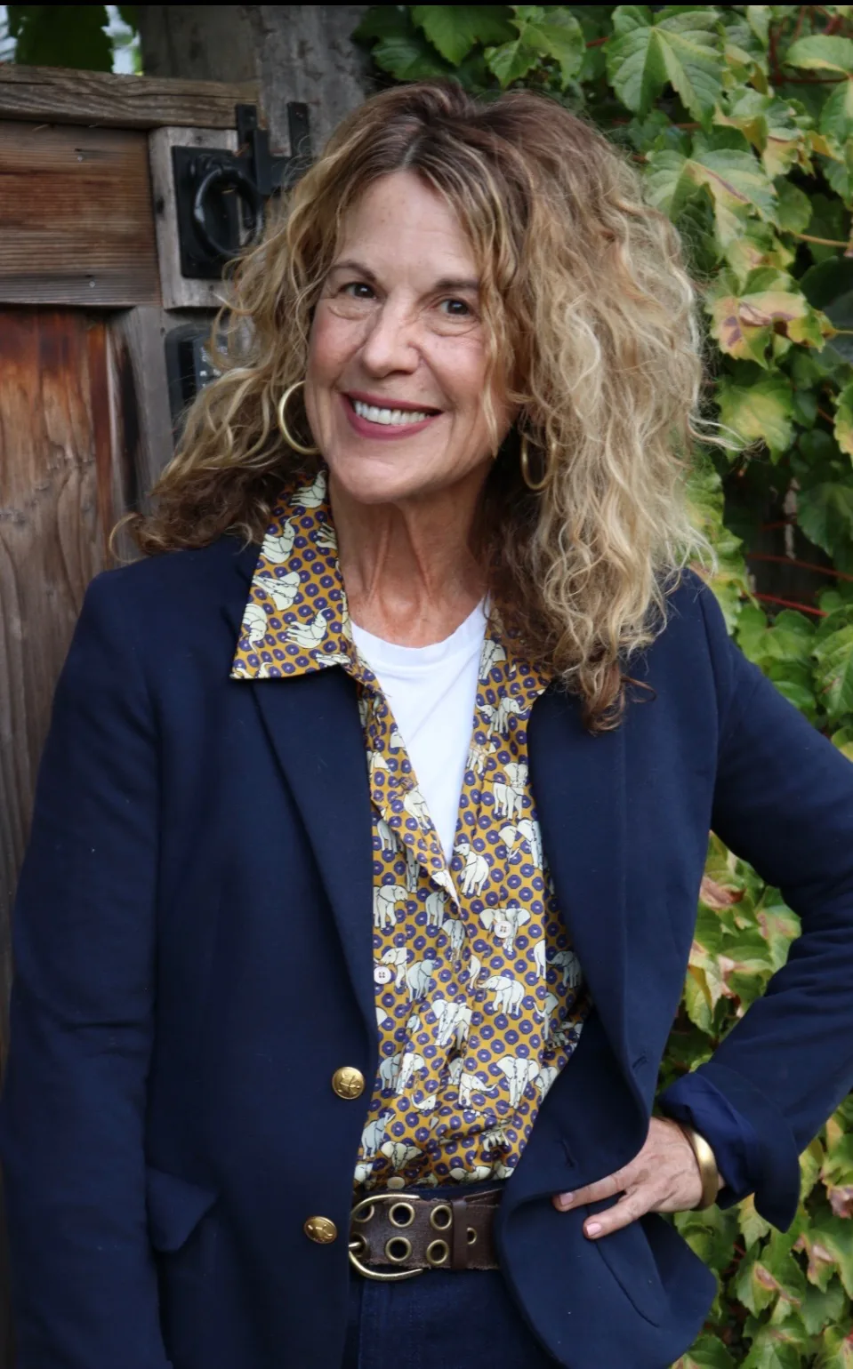 Sharon Davis, smiling, outdoors against a weathered fence and ivy.